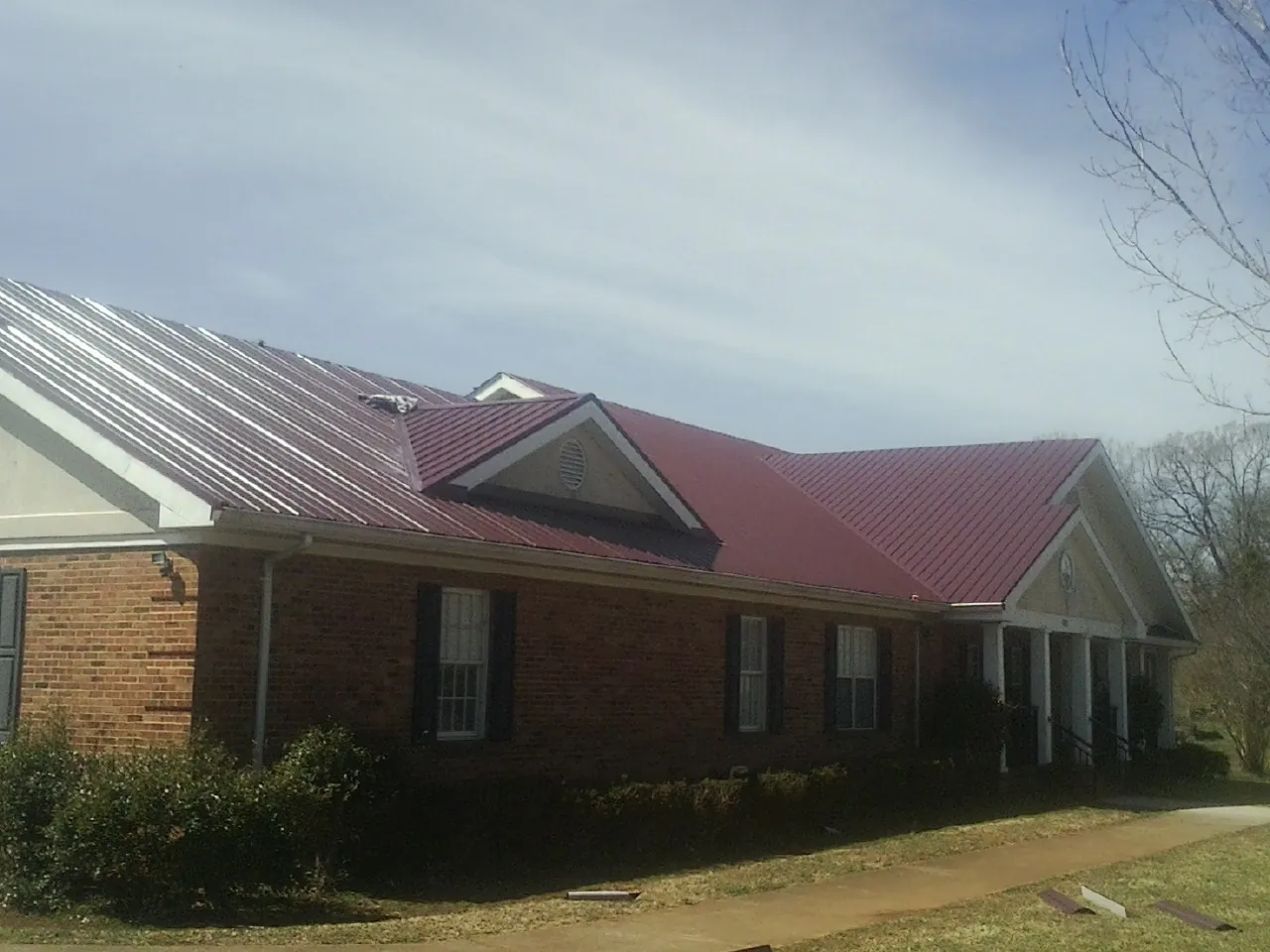 Red metal roof with gabled entries on a long brick building, from a Hail Damage Roof Repair job in Gaston