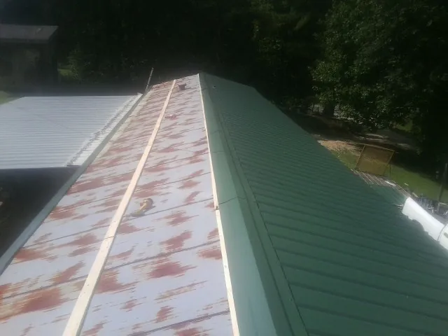 Old rusted panels beside newly installed green metal roofing — Wind Damage Roof Repair by Roofing Brothers in Gaston