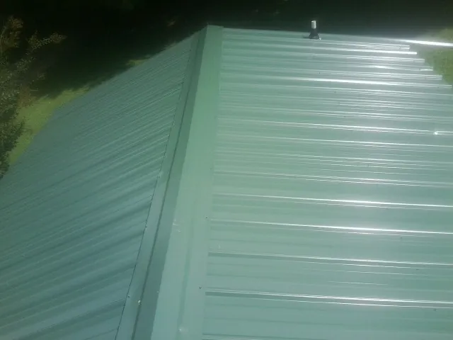 New green metal panels meeting at the ridge of a roof — Flat Roof Repair work by our crew in Gaston
